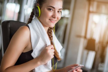 Kulaklıkla müzik dinleyen genç ve çekici bir kadın akıllı telefona bağlanıyor. Spor salonunda sıkı çalıştıktan sonra rahatlama.