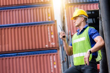 Telsiz iletişimi ya da telsiz kullanarak, sarı güvenlik kaskı takarak ve kargo nakliye gemisinden ithalat ve ihracat için konteynır kutusunu kontrol ederek kendine güvenen beyaz adam mühendisi. 