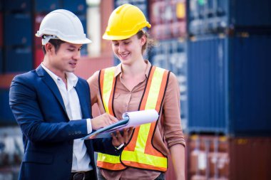 Mühendis konteynır deposunda sabit kasklı bir kargo taşıyor ve kargo nakliye gemisinden ithalat ve ihracat için konteynır kutusunu kontrol ediyor. Takım çalışması konsepti 