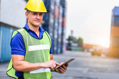 Dijital tablet kullanan ve sarı kasklı genç, kendine güvenen beyaz adam mühendisi. İthalat ve ihracat için Kargo nakliye gemisinden konteynır kutusunu kontrol et.. 