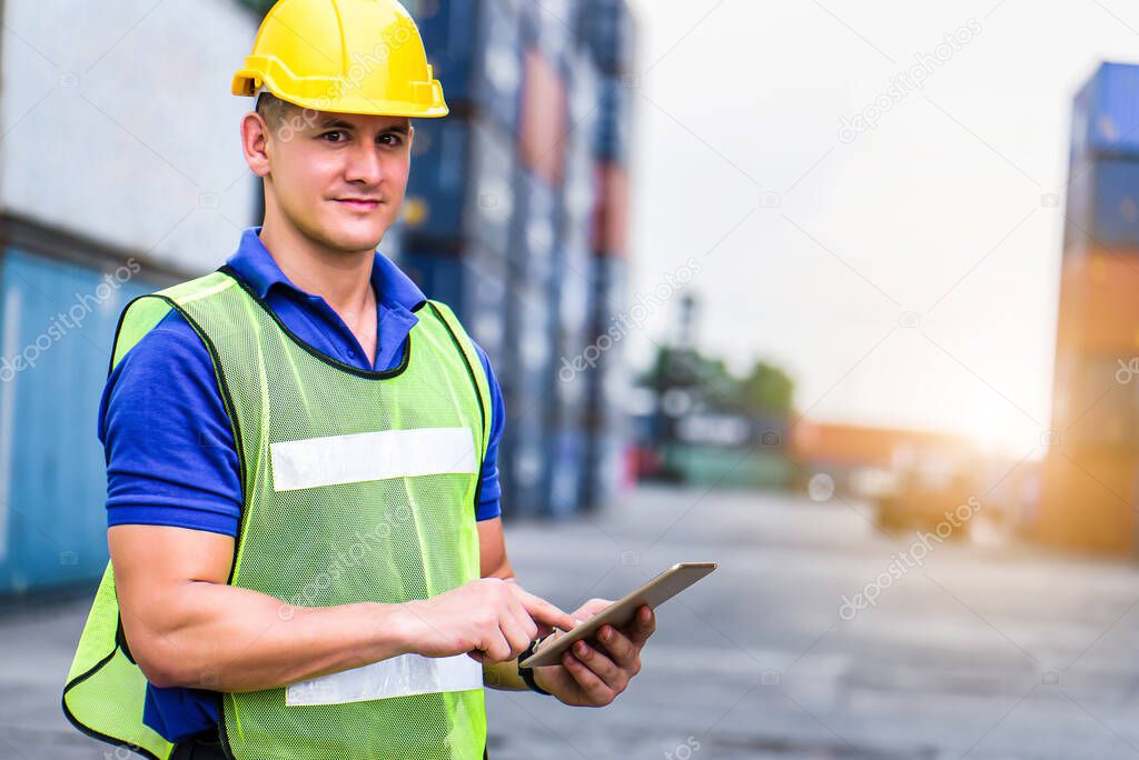 Young confident Caucasian man engineer using digital tablet and wearing yellow safety helmet and check for control loading containers box from Cargo freight ship for import and export, transport. 