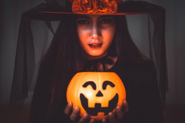 Cadı gibi giyinmiş çekici bir Asyalı kadın elinde balkabağı feneriyle Cadılar Bayramı tatilini sinematik ve karanlık bir tonda tutuyor..