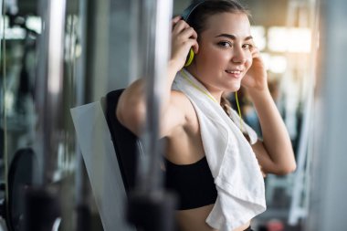 Genç, beyaz bir kadın akıllı telefon ya da cep telefonuna bağlı kulaklıkla müzik dinliyor. Spor salonunda sıkı çalıştıktan sonra rahatlama. 