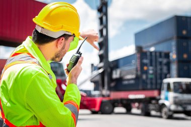 Kafkasyalı mühendis sarı güvenlik kaskı takıyor. Telsizle şoförü ara ve kargo gemisinden ithalat ve ihracat için konteyner yükleme kutusunu kontrol et.  