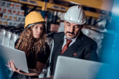 Mühendis kadın ve işadamı yük deposunda sabit kasklı bir kargo taşıyorlar ve dizüstü bilgisayardan gelen rapora göre ithalat ve ihracat için kargo gemisinden yükleme kontrolü yapıyorlar. Takım çalışması konsepti 