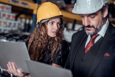 Mühendis kadın ve işadamı yük deposunda sabit kasklı bir kargo taşıyorlar ve dizüstü bilgisayardan gelen rapora göre ithalat ve ihracat için kargo gemisinden yükleme kontrolü yapıyorlar. Takım çalışması konsepti 