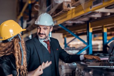 Mühendis kadın ve işadamı yük deposunda sabit kasklı bir kargo taşıyorlar ve dizüstü bilgisayardan gelen rapora göre ithalat ve ihracat için kargo gemisinden yükleme kontrolü yapıyorlar. Takım çalışması konsepti 