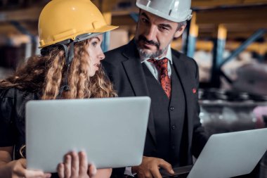 Mühendis kadın ve işadamı yük deposunda sabit kasklı bir kargo taşıyorlar ve dizüstü bilgisayardan gelen rapora göre ithalat ve ihracat için kargo gemisinden yükleme kontrolü yapıyorlar. Takım çalışması konsepti 