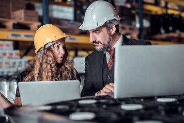 Mühendis kadın ve işadamı yük deposunda sabit kasklı bir kargo taşıyorlar ve dizüstü bilgisayardan gelen rapora göre ithalat ve ihracat için kargo gemisinden yükleme kontrolü yapıyorlar. Takım çalışması konsepti 