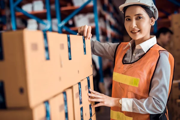Confident Asian woman owner standing and crossed her arm at goods warehouse store and check for control loading containers box from Cargo freight ship for import and export