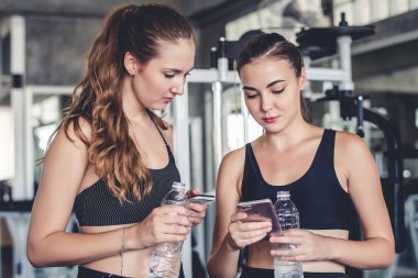 Spor salonunda sıkı çalıştıktan sonra rahatlarken akıllı telefon ya da cep telefonu kullanan iki çekici kadın.  