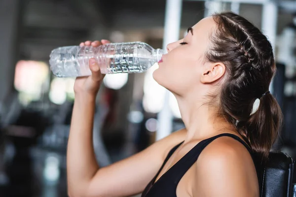 Attractive young Caucasian beautiful woman get resting and drink some water from plastic bottle after workout at gym