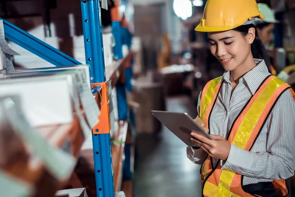 Engineer warehouse woman wearing a hardhat standing cargo at goods warehouse and check for control loading from Cargo freight ship for import and export by report on tablet. Teamwork concept