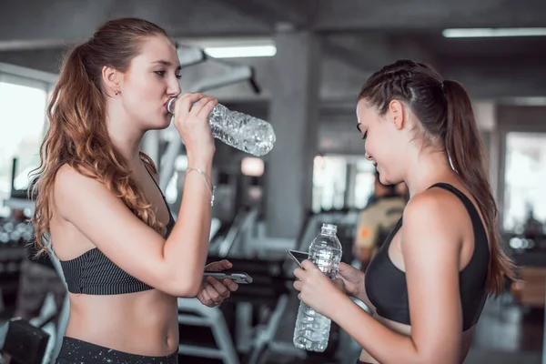 Spor salonunda sıkı çalıştıktan sonra rahatlarken akıllı telefon ya da cep telefonu kullanan iki çekici kadın. 