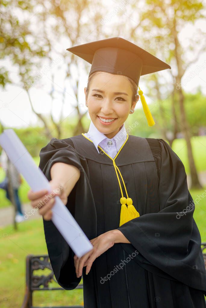 Graduated woman students wearing graduation hat and gown with happiness feeling with park background