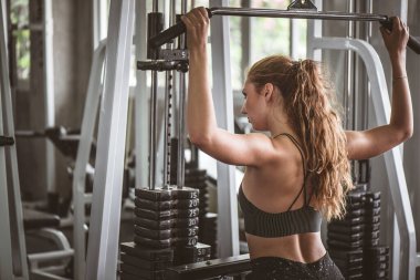 Genç ve çekici bir jimnastik makinesiyle egzersiz yapan çekici bir kadının sinematik tonu. Vücut kaslarını sağlıklı yaşam konseptine uydurmak için bireysel spor 