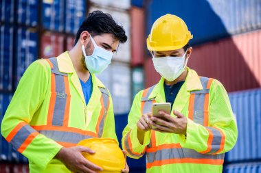 Genç mühendis cep telefonu kullanıyor ve sarı güvenlik kaskı takıyor. İthalat ve ihracat için kargo gemisinden konteynır kutusunu kontrol ediyor. takım çalışması konsepti. 