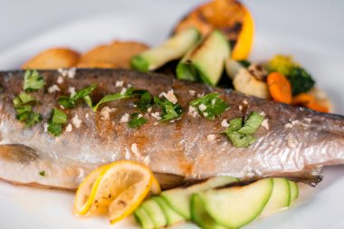 Fırında alabalık, patates, ızgara sebze ve tabakta limon.