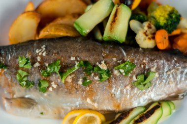 Fırında alabalık, patates, ızgara sebze ve tabakta limon.