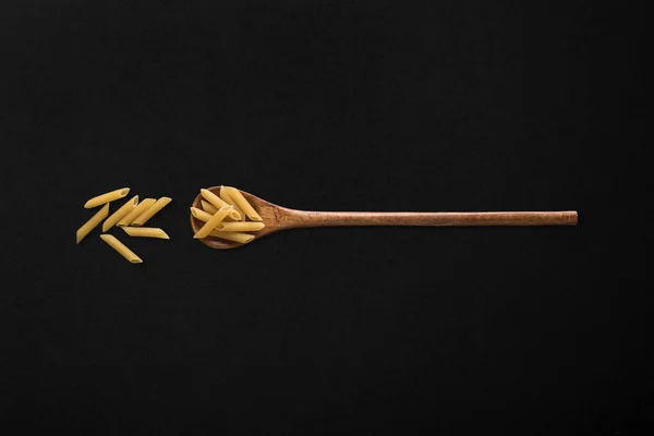 Siyah arka planda tahta kaşıkta makarna.
