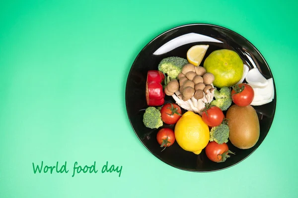 World food day, vegetarian day or healthy food concept. Fresh vegetables and fruits on black plate on green background. Top view