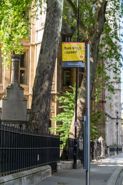Fetter Lane, Londra 'daki otobüs durağı Coronavirus COVID-19 sosyal uzaklık gereksinimleri nedeniyle çok eski ve büyük Elm Ağaçları güneşli bir günde arka planda.
