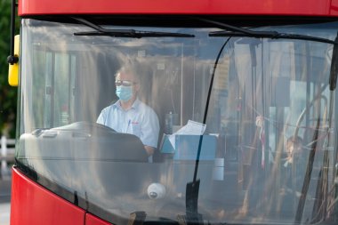 Waterloo Köprüsü, Londra, İngiltere 'de Coronavirus COVID-19 pandemik tecrit sırasında güvenlik bandı ve maske takan çift katlı kırmızı bir Londra otobüsünün sürücüsü - 2