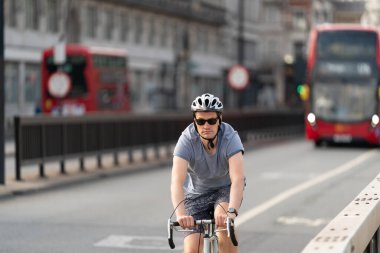 Londra Waterloo Köprüsü 'nde bisiklet yolunda bisiklet süren genç bir bisikletçi Coronavirus COVID-19 salgınında kask takıyor.
