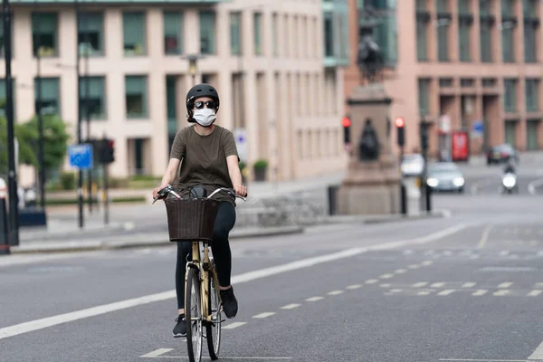 Coronavirus COVID-19 salgınında maske takarak Holborn, Londra 'da otobüs yolunda bisiklet süren genç bir kadın.