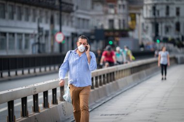 Londra, İngiltere 'de Waterloo Köprüsü' nde yürüyen ve COVID-19 salgını sırasında cep telefonuyla konuşan orta yaşlı bir adam.