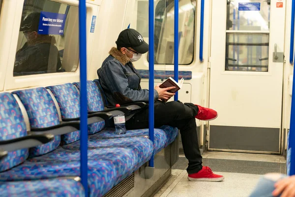 COVID-19 Coronavirus salgını sırasında maske takan genç bir adam Piccadilly Hattı 'ndaki Londra metro vagonunda.