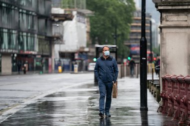 Londra, Holborn, Londra 'da COVID-19 salgını sırasında yağmurda yağmurlu bir günde maske takarken yakalanan iş adamı.