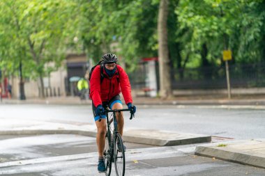 10 Haziran 2020 'de Londra, Holborn' daki COVID-19 salgını sırasında yağmur damlacıklarıyla kaplı bir kask takan ve çiselemeli bir günde bisiklet süren genç bir bisikletçi.