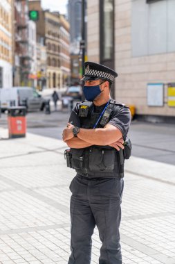 3 Temmuz 2020 'de Farringdon İstasyonu' nun dışında görevli erkek polis memuru maske takıyor ve Londra metrosunda sosyal mesafeleri belirleme kurallarını uyguluyor.