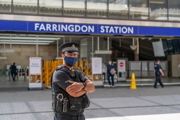 3 Temmuz 2020 'de Farringdon İstasyonu' nun dışında görevli erkek polis memuru maske takıyor ve Londra metrosunda sosyal mesafeleri belirleme kurallarını uyguluyor.