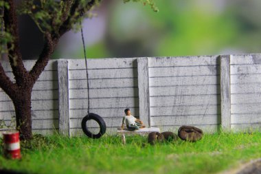 Minik oyuncak Endonezyalı orta yaşlı adam sarung ve beyaz gömlek giyiyor, büyük ağacın altında dinleniyor.