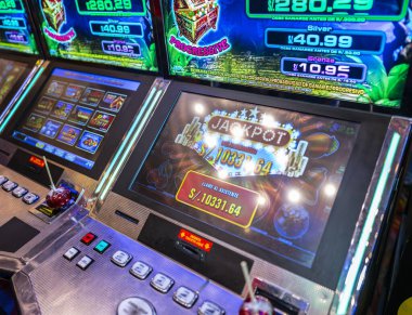 Lima, Peru, 31 Ağustos 2023: Kumarhanenin içinde yanan düğmelerle büyük ikramiye ekranını gösteren slot makinesinin yakın çekimi. Bir elma şekeri makinenin üzerinde duruyor, kumar yaşam tarzını şenlikli atıştırmalık kültürüyle karıştırıyor. Gece hayatını ve eğlenceyi temsil eder..