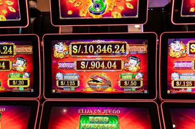 Lima, Peru, 30 Eylül 2023: Fortunes 3 logosunu altın sikkeler ve parlak grafiklerle gösteren bir kumarhane slot makinesinin yakın çekimi. Dijital ekranda modern bir oyun salonunda ikramiye, şans ve heyecan vurgulanıyor.