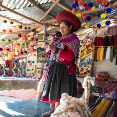 Cusco, Peru, 12 Ağustos 2022: Peru 'nun Cusco kentinde yün ören yerli kadın. Renkli hikayeleri ve kültürel mirası olan geleneksel tekstil işçiliği.