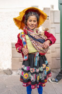 Cusco, Peru, 12 Ağustos 2022: Cusco, Peru 'da gülümseyen And kızı, geleneksel işlemeli etek ve renkli dokuma ürünleri giymiş, bir bebek kuzu taşıyor. Bu otantik kültürel portre Keçuva mirası ve Andean geleneklerini temsil ediyor..