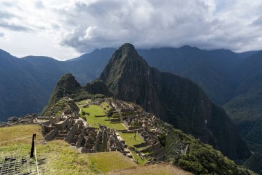 Machu Picchu 'nun Huayna Picchu dağının arkasında yükseldiği panoramik manzarası. Cusco, Peru 'daki UNESCO Dünya Mirası bölgesi İnka medeniyetinin simgelerinden ve en simgelerinden biridir..