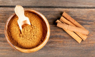 Tarçın çubukları ve tarçın tozu ahşap arka planda kasede.