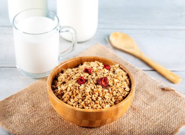 Yuvarlanmış yulaf ezmesi ya da ahşap kaşıklarla kasede yulaf ezmesi ve arka planda bir şişe süt..