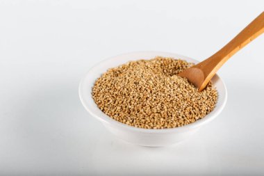 Beyaz arka planda kaşık ve kase ile kinoa taneleri