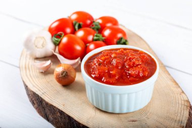 Sarımsaklı domates sosu, fesleğen ve baharatlar ahşap arka planda beyaz bir kasede..