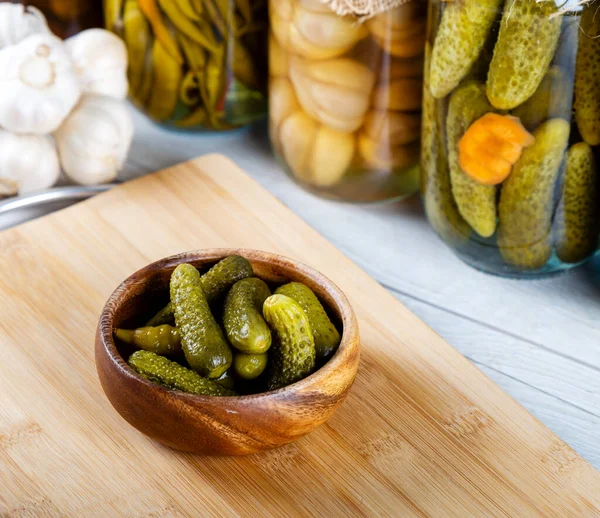 Bowl of pickled cucumbers and jars of pickled vegetables on wooden background