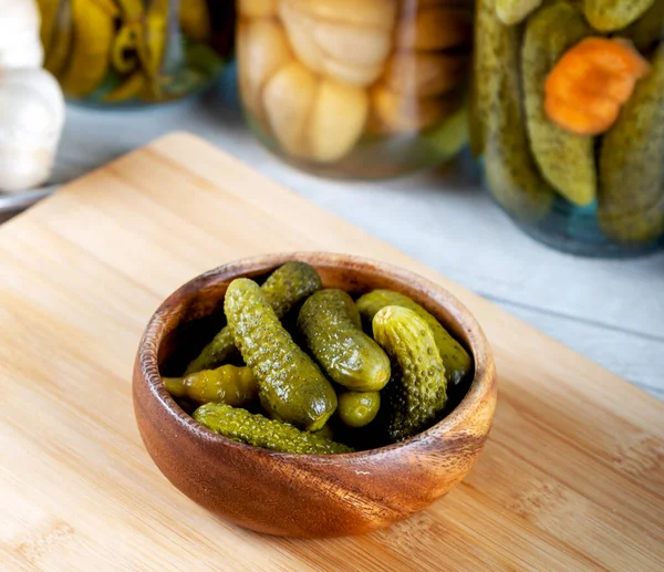 Bowl of pickled cucumbers and jars of pickled vegetables on wooden background