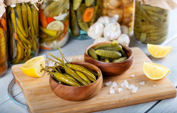 Bowl of pickled cucumbers, green peppers and jars of pickled vegetables