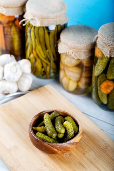 Bowl of pickled cucumbers and jars of pickled vegetables on wooden background