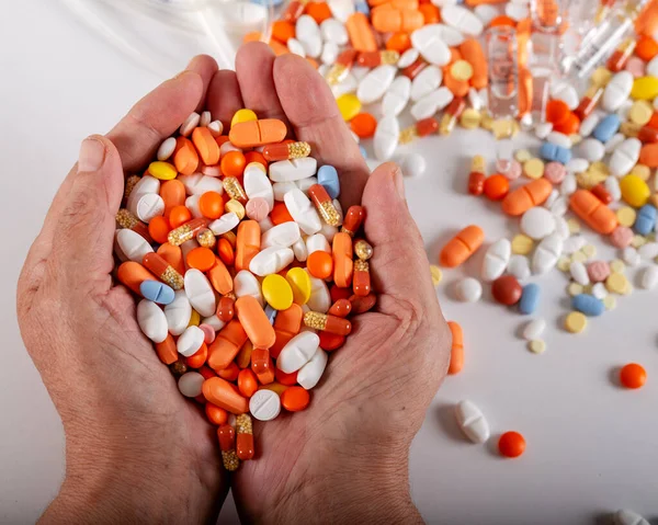 Yaşlı bir kadın, beyaz bir arka planda yaşlı ellerde bir sürü renkli hap tutuyor. Acı dolu bir ihtiyarlık. Yaşlıların sağlık hizmetleri.